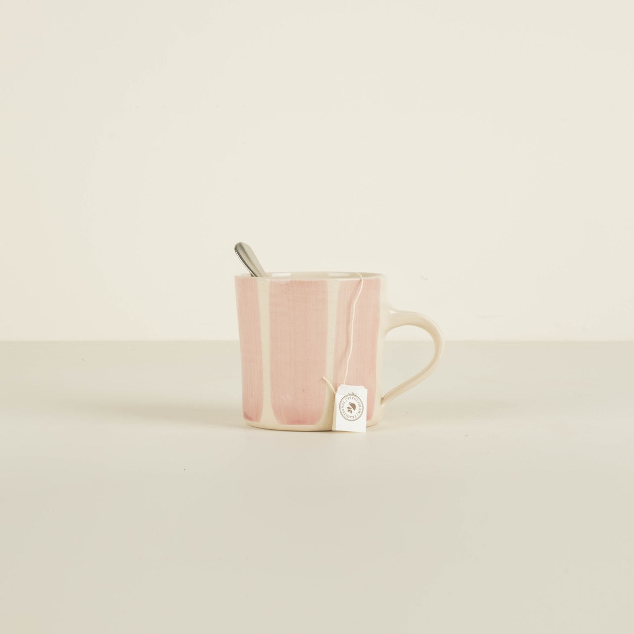 Pink ceramic mug with a tea bag and spoon on a beige background
