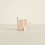 Pink ceramic mug with a tea bag and spoon on a beige background