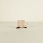 Pink and white ceramic mug with a small amount of coffee grounds on a beige background