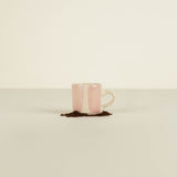 Pink and white ceramic mug with a small amount of coffee grounds on a beige background