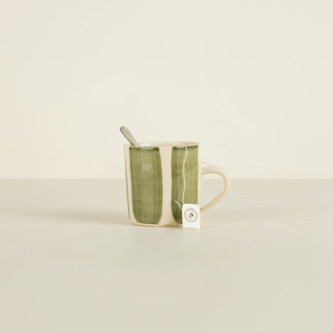 Green ceramic mug with a spoon on a beige background