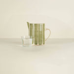 Green ceramic pitcher and glass of water on a beige surface