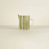 Green and white ceramic pitcher on a beige background