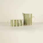 Two ceramic pitchers with green and white striped pattern on a beige background