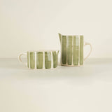 Two ceramic pitchers with green and white striped pattern on a beige background