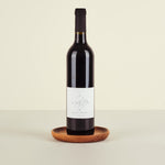 Red wine bottle on a wooden coaster with a beige background
