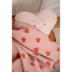 Heart-shaped pillow with a smiley face and pink blanket with hearts on a white background