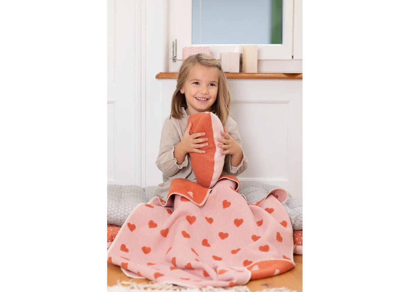 Child holding a heart-patterned blanket in a home setting