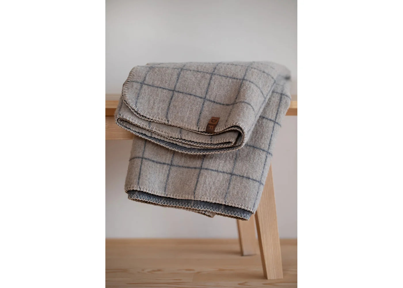 Plaid blanket draped over a wooden stool against a white wall