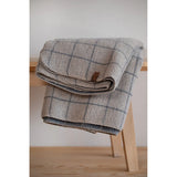 Plaid blanket draped over a wooden stool against a white wall