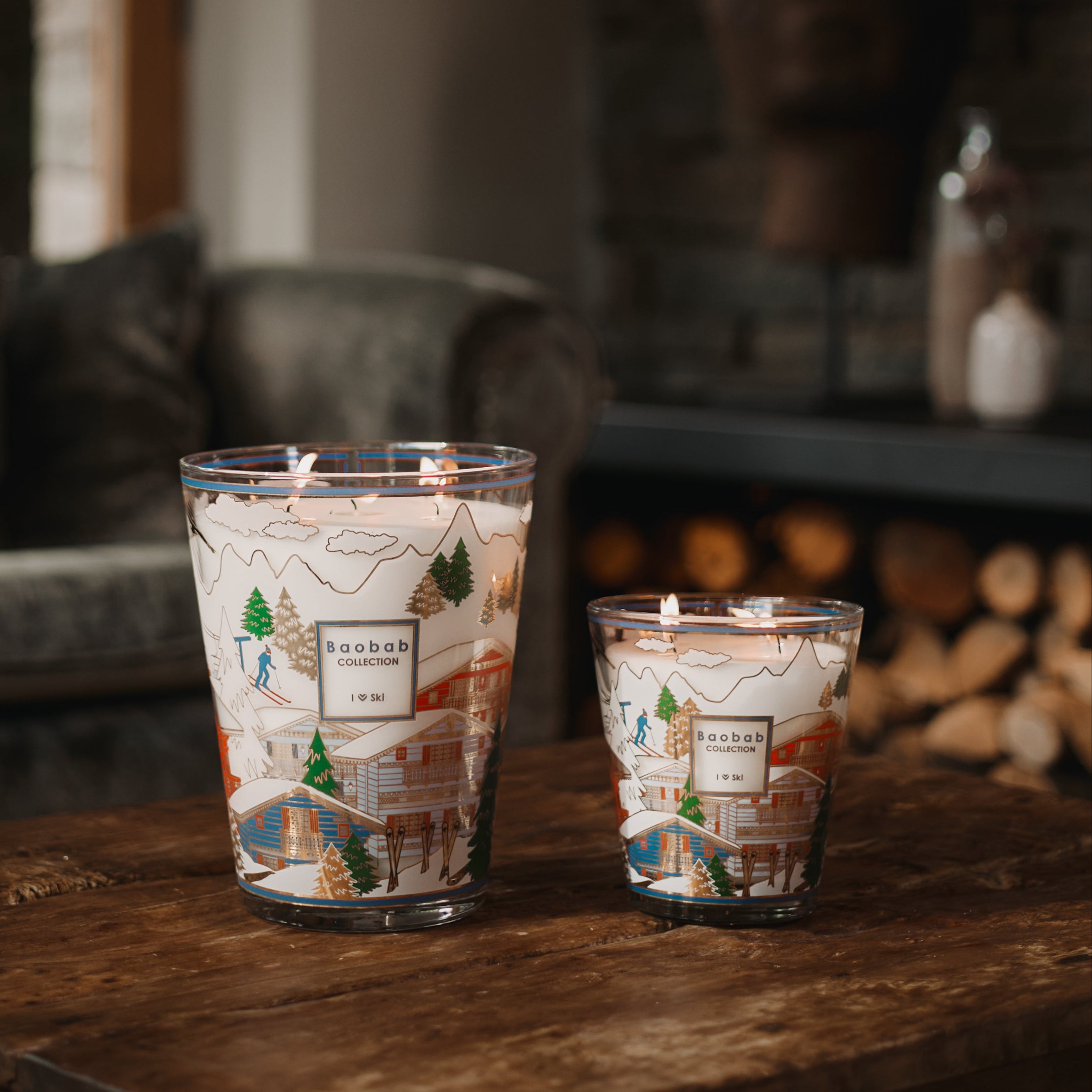 Two candles with decorative labels on a wooden surface in a cozy indoor setting.