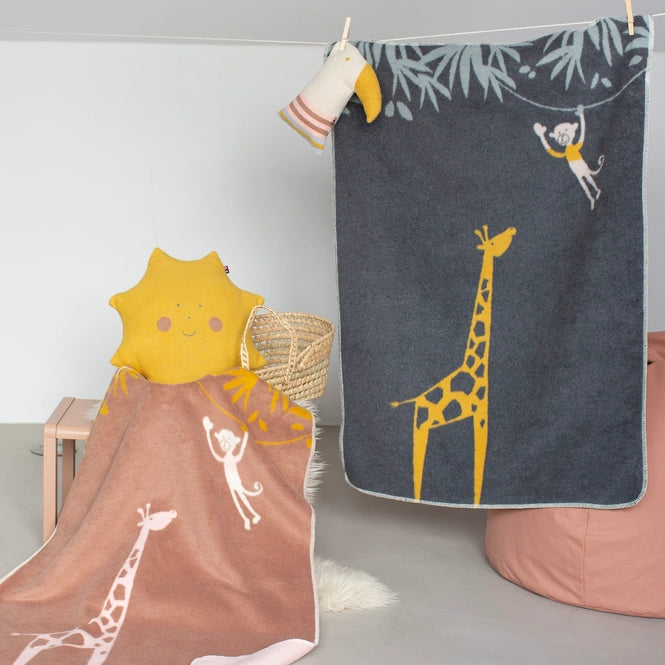 Children's blankets with giraffe designs hanging on a line against a light gray wall.