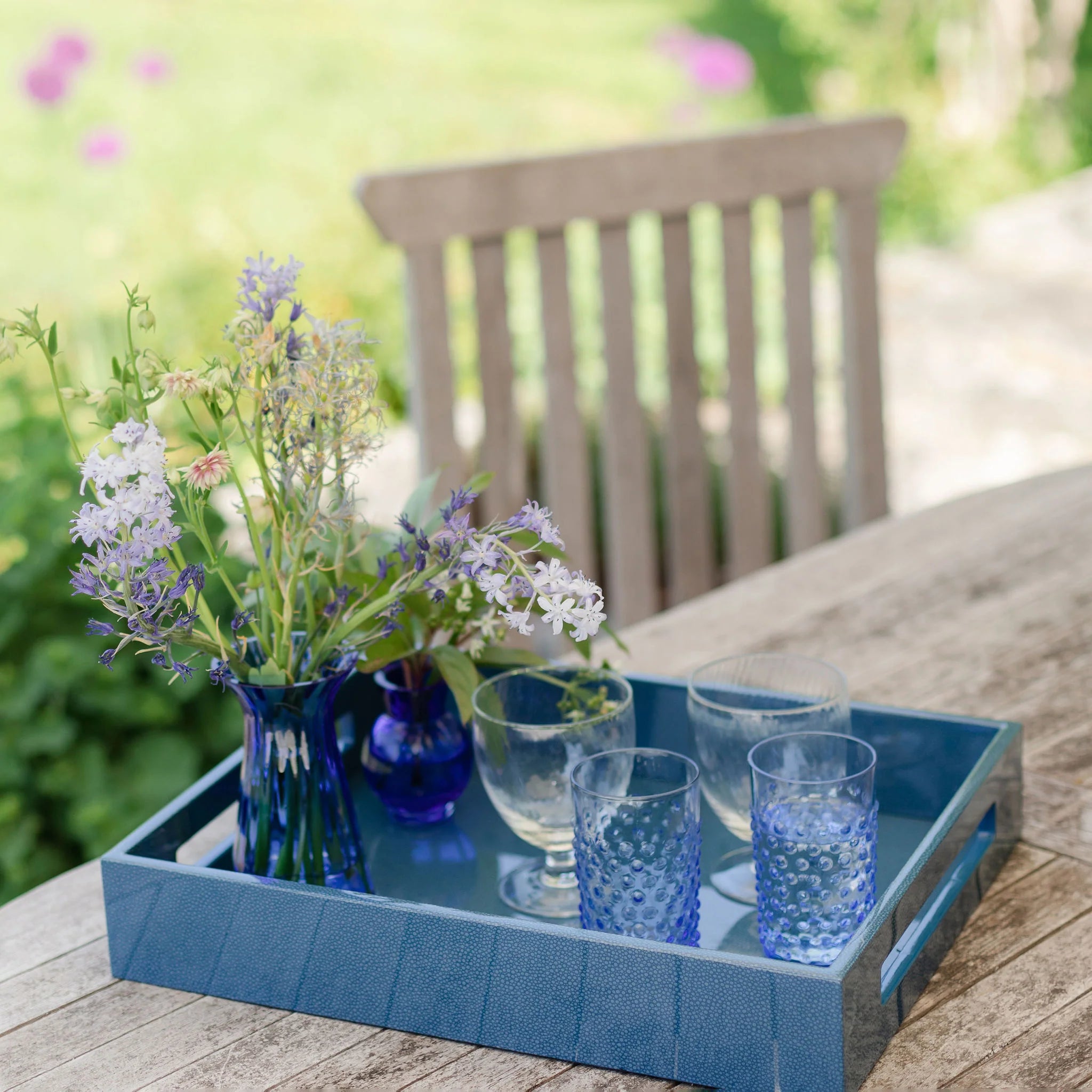 Blue shagreen tray with glasses and flowers on a wooden table outdoors