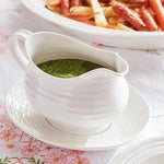 White gravy boat with green sauce on a floral tablecloth