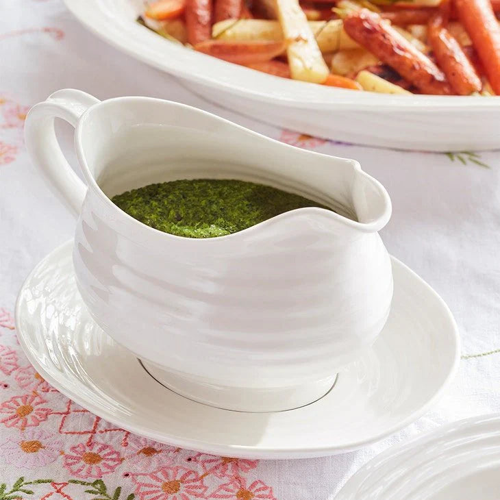 White gravy boat with green sauce on a floral tablecloth
