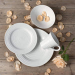 White ceramic plates and mug on a wooden surface with scattered petals and a rose.
