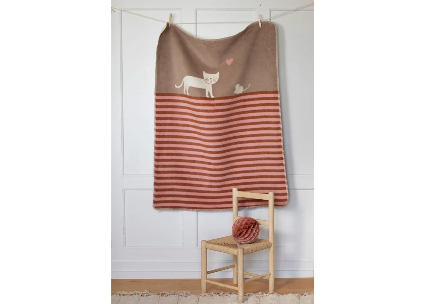 Striped towel with cat design hanging on a line against a white wall.