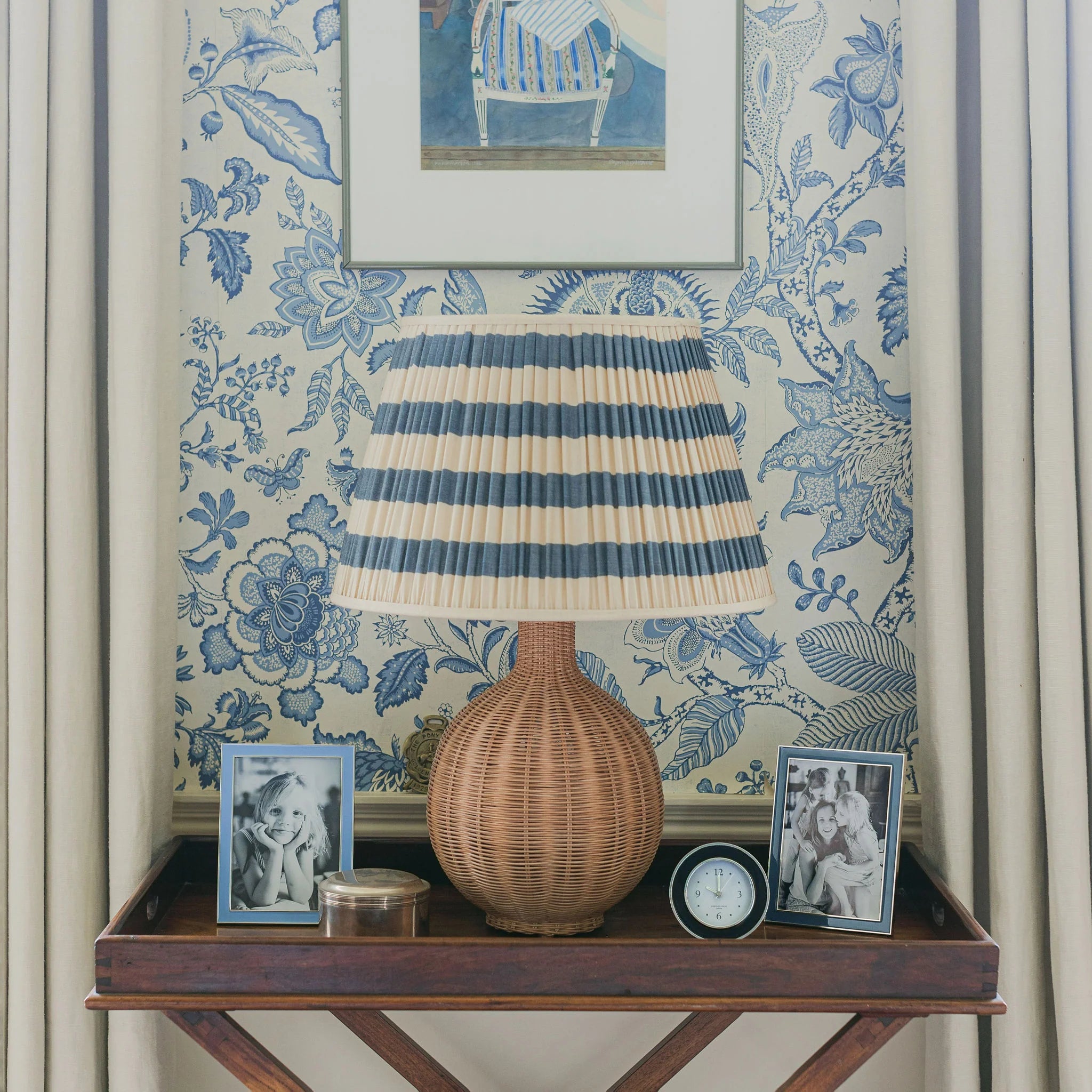 Decorative table with lamp, denim silver picture frames, and clock against floral wallpaper