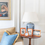 Living room corner with a beige sofa, blue pillow, side table with decorative items, orange silver picture frames and wall art.