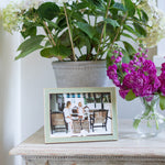 Sage silver framed photo of a couple on a table with flowers and a plant in the background