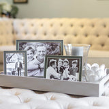 Three black and white taupe silver photo frames on a decorative tray with a blurred background