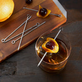 Cocktail with garnish on a wooden board with skewers and an orange slice.